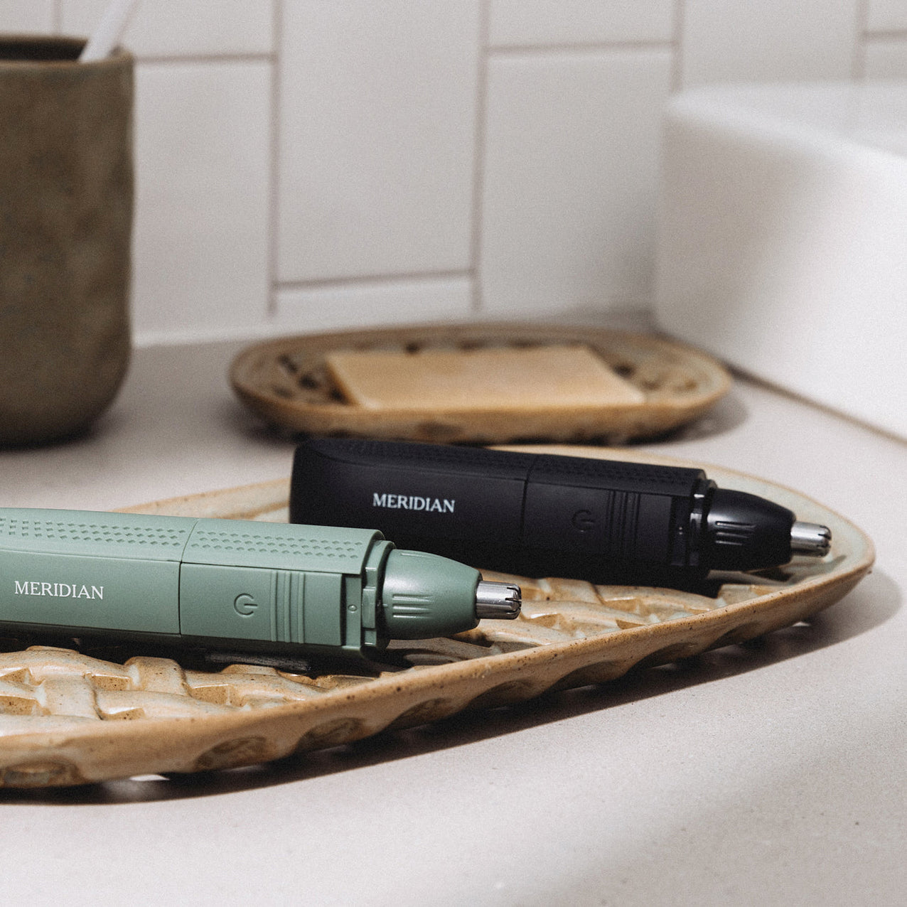 Two Meridian branded electric grooming trimmers in black and green, placed on a decorative beige tray on a bathroom countertop.