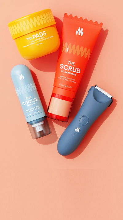 A flat lay of Meridian grooming products including a yellow jar of pads, an orange tube of scrub exfoliator, a blue bottle of daily soothing spray, and a blue electric grooming tool on a peach background.