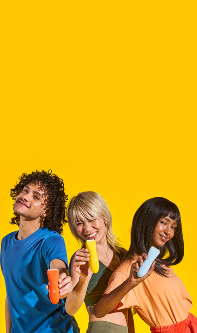 Three diverse models smiling and holding colorful Meridian grooming trimmers against a bright yellow background.