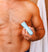 Man grooming chest hair with blue electric body hair trimmer in wooden bathroom with white towel hanging.
