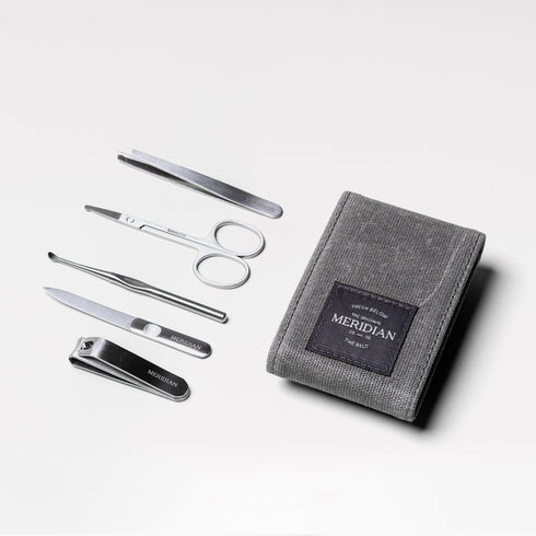 Men's grooming kit with stainless steel nail clippers, scissors, tweezers, nail file, and cuticle pusher next to a grey textured pouch labeled Meridian.