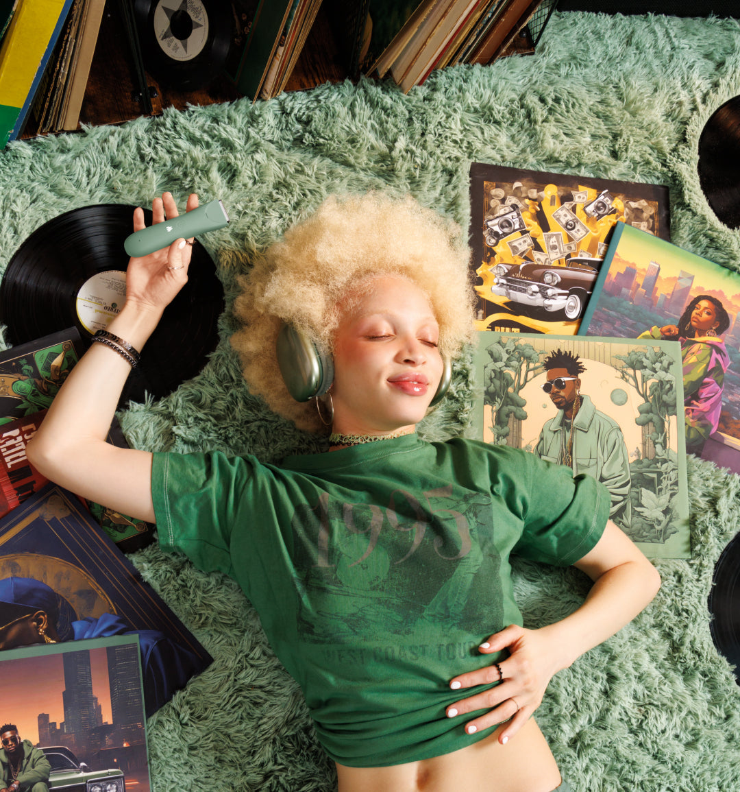 Blonde woman with curly hair in green shirt listening to vinyl records with headphones on green shag carpet